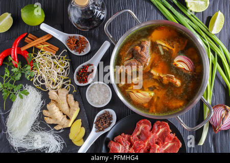 Bestandteile von vietnamesischen soup Pho Bo, mit rohem Fleisch, Knochen Brühe in einen Edelstahl Pfanne, Soja Sprossen, Gewürze, gebackene Zwiebel, Reis, Nudeln, frischem Koriander ein Stockfoto