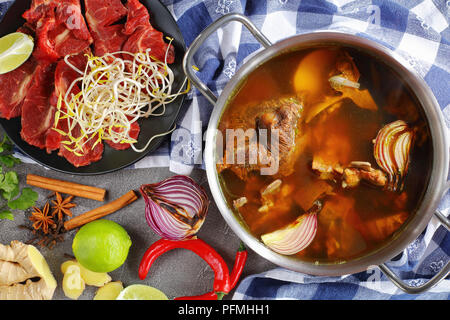 In der Nähe der heißen Brühe Rindfleisch mit Knochen und andere Zutaten für traditionelle vietnamesische Suppe Pho Bo mit rohem Rindfleisch, Sojasprossen, Gewürze und Grüns, Ansicht von Stockfoto