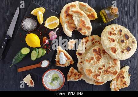 Frisch gebackenes Fladenbrot auf schwarzer Holztisch mit herzhaften tzatziki Soße Zutaten auf Stein Schneidbrett, horizontale Ansicht von oben Stockfoto