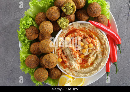 In der Nähe von köstlichen Falafelkugeln auf Platte mit Hummus in eine Schüssel, Chili Peppers und Salatblätter, klassisches Rezept, horizontale Ansicht von oben Stockfoto