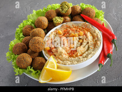 In der Nähe von köstlichen Falafelkugeln auf Platte mit hausgemachten Hummus mit rotem Pfeffer und Olivenöl in eine Schüssel sprengte, Chili Peppers und Salatblätter, Stockfoto