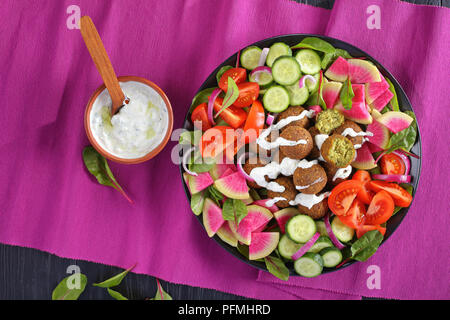 Frittierte Falafelkugeln auf Platte mit Gemüse bunter Salat von Wassermelone Rettich, Mangold Blätter, Gurken- und Tomatenscheiben. tzatziki Sauce in der Schüssel Stockfoto