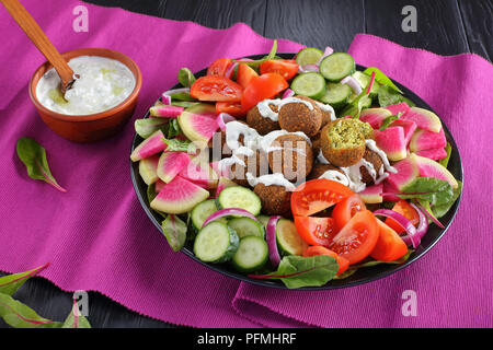 Lecker Falafelkugeln auf Platte mit Gemüse bunter Salat von Wassermelone Rettich, Mangold Blätter, Gurken- und Tomatenscheiben. tzatziki Sauce in der Schüssel, vie Stockfoto