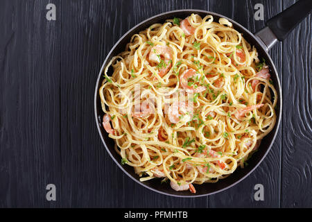 Creamy Shrimp Alfredo linguine bestreut mit fein gehackter Petersilie in Skillet auf schwarzen Holztisch, einfaches Rezept, von oben betrachten Stockfoto