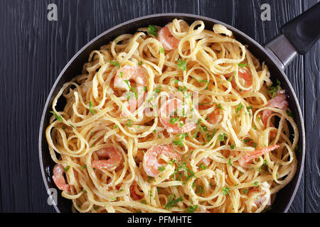 Lecker einen Topf Abendessen - Creamy Shrimp Alfredo Pasta mit gehackter Petersilie in Skillet auf schwarzen Holztisch sprengte, Ansicht von oben Stockfoto