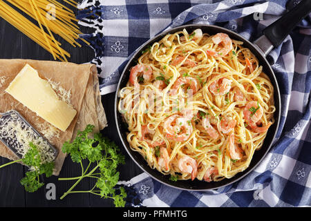 Köstliche cremige Parmesan Linguine mit Shrimps bestreut mit fein gehackter Petersilie in Skillet auf schwarzer Holztisch mit Stück Käse und uncook Stockfoto