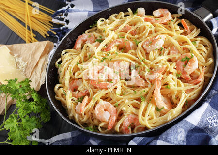 Köstliche cremige Parmesan Linguine mit Shrimps bestreut mit fein gehackter Petersilie in Skillet auf schwarzer Holztisch mit Stück Käse und uncook Stockfoto