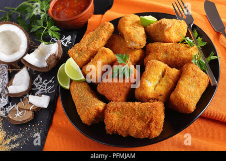 In der Nähe von köstlichen Stück weißen Fisch, beschichtet mit Kokosnuss Brotkrumen und gebraten. Zutaten und hausgemachten mango Sauce im Hintergrund, Blick von Stockfoto