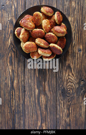 Lecker gebratene Koteletts aus forcemeat, geriebenen Kartoffeln, Zwiebeln und Gewürzen auf schwarze Platte, auf alten verkohlten Holztisch, vertikale Ansicht von oben Stockfoto