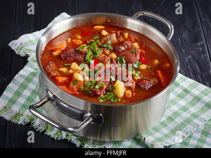 In der Nähe von köstlichen heißen Ungarisches Gulasch mit Rindfleisch, Paprika, Gemüse und csipetke - kleine Eiernudeln in Edelstahl Kasserolle auf Schwarz Stockfoto