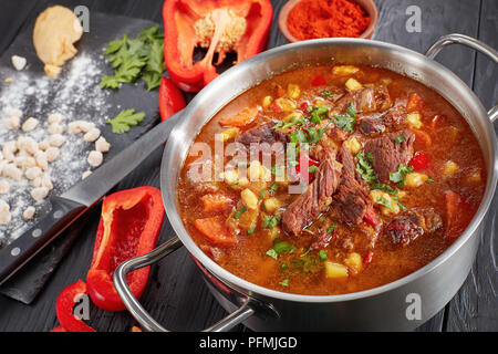 In der Nähe von Hot Rindfleisch ungarischen Gulasch oder bograch Suppe mit Paprika, kleine Eier Nudeln, Gemüse und Gewürzen in einen Topf. Zutaten und Suppenkelle auf Stockfoto