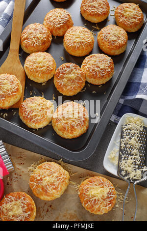 Frisch gebackene leckere englische Scones mit geriebenem Käse bestreut auf Backblech, vertikale Ansicht von oben Stockfoto
