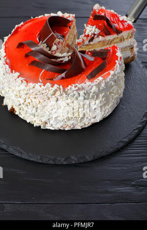 Köstliche Torte mit Frischkäse Mousse dekoriert mit weißer Schokolade Flocken, roten Beeren Marmelade und Schokolade Chips auf schwarzem Schiefer Teller mit Stockfoto