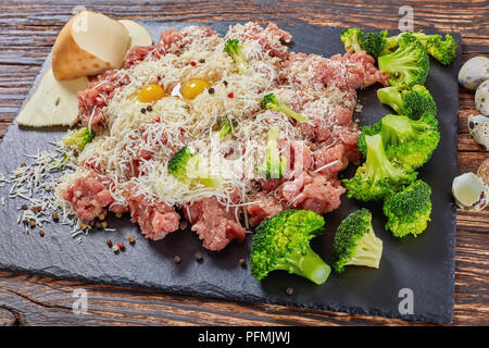 Rohe frische forcemeat bestreut mit Panko Paniermehl, geriebenem Käse und gekochten Brokkoli, Eier und Gewürze Fleisch Kugeln auf Stein Fach auf Holz zu machen Stockfoto