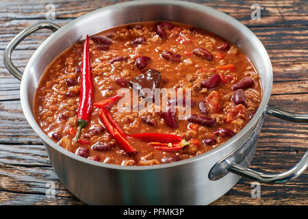 In der Nähe von Hot leckeres Chili con carne mit ganzen Red Hot Chili, Bohnen, Tomaten und ein Stück Schokolade in einem Topf auf rustikalen Holztisch, Ho Stockfoto
