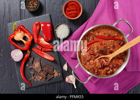 Ein leckeres Chili con carne mit ganzen Red Hot Chili, Bohnen, Tomaten und ein Stück Schokolade in einem Topf mit Zutaten im Hintergrund, horizo Stockfoto