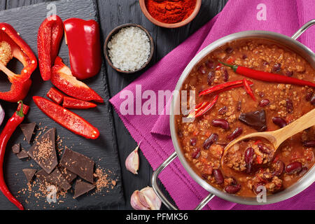 Ein leckeres Chili con carne mit ganzen Red Hot Chili, Bohnen, Tomaten und ein Stück Schokolade in einem Topf mit Zutaten im Hintergrund, horizo Stockfoto