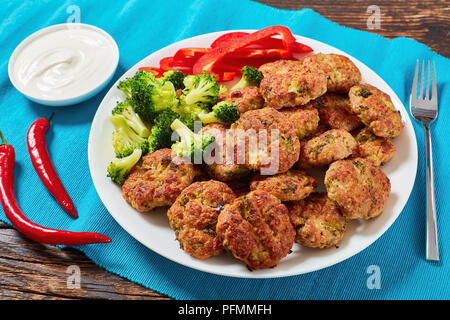 Im Ofen gebackenes Geflügel saftig Brokkoli Frikadellen gefüllt mit geriebenen Käse auf weiße Platte serviert mit saurer Sahne in der Schüssel auf alten Holztisch, gesund Stockfoto