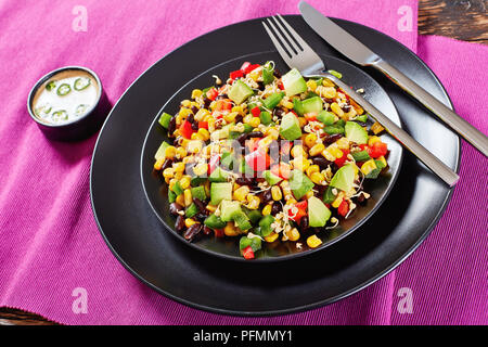 In der Nähe des mexikanischen Stil Salat mit Avocado, schwarze Bohnen, Dose Mais, Buchweizen Sprossen, gewürfelte rote und grüne Pfeffer auf schwarzem Teller serviert mit SILV Stockfoto