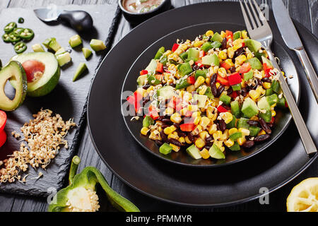 In der Nähe des mexikanischen wenig Kalorien Salat mit Avocado, schwarze Bohnen, Maiskörner, Buchweizen Sprossen, gewürfelt Pfeffer auf Schwarze Platten mit Zutat serviert. Stockfoto