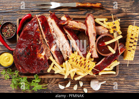 Lecker saftig Hausgemachten geräucherten Grill Rippchen fallen aus den Knochen auf Schneidebrett mit Pommes frites, gegrillte Maiskolben, Barbecue Sauce und mustar Stockfoto