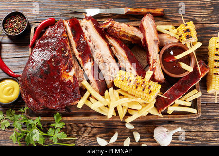 Lecker saftig hausgemachten Grill Gebratene Rippchen fallen aus den Knochen auf Holz Schneidebrett mit Pommes frites, gegrillte Maiskolben, Barbecue Sauce ein Stockfoto
