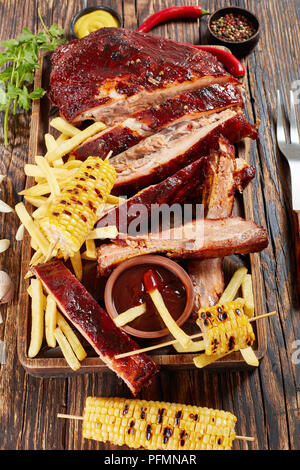 Lecker saftig hausgemachten Grill Gebratene Rippchen fallen aus den Knochen auf Holz Schneidebrett mit Pommes frites, gegrillte Maiskolben, Barbecue Sauce ein Stockfoto