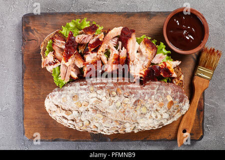 Nahaufnahme der leckere saftige riesen BBQ Rib Sandwich von Roggenbrot Brot mit frischen grünen Salat, Schweinefleisch in Scheiben geschnitten und leckeren hausgemachten Grill sa Stockfoto