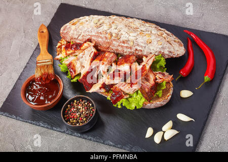 Nahaufnahme der leckere saftige riesen BBQ Rib Sandwich von Roggenbrot Brot mit frischen grünen Salat, zerkleinertem Schweinefleisch, und leckere hausgemachte Barbecue Sauce, Stockfoto