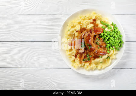 Leckere Würstchen mit Kartoffelbrei - saftig gebraten heiße Würstchen mit braunen Kruste in dicke Zwiebel Soße mit Kartoffelpüree und grünen Erbsen, klassisches Rezept, Anzeigen Stockfoto