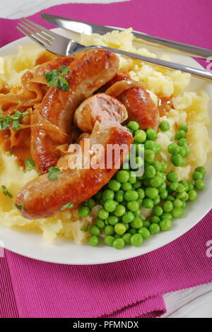 Leckere Würstchen mit Kartoffelbrei - saftig gebratene Würstchen in Lasten des Onion gravy Ertrinken, mit sahnigem Kartoffelpüree und grünen Erbsen, klassisches Rezept, Verti Stockfoto