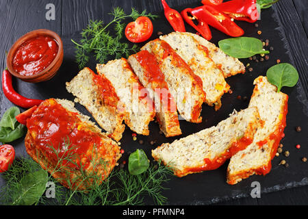 Köstlich gebackenen Fisch terrine Schichten serviert mit Pfeffer, frische Grün und Tomatensauce auf schwarzem Schiefer Board auf Holztisch, vertikale Ansicht von oben, Stockfoto