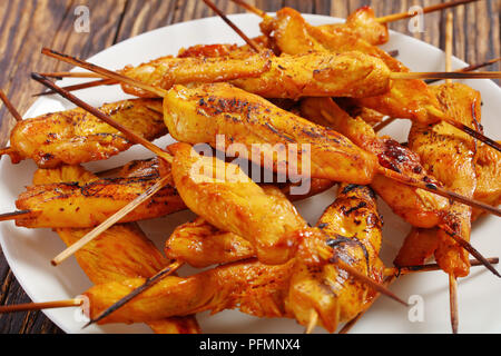 Chicken Satay auf Spieße auf einem weißen Teller auf Holztisch, authentische Rezept, Ansicht von oben, close-up Stockfoto