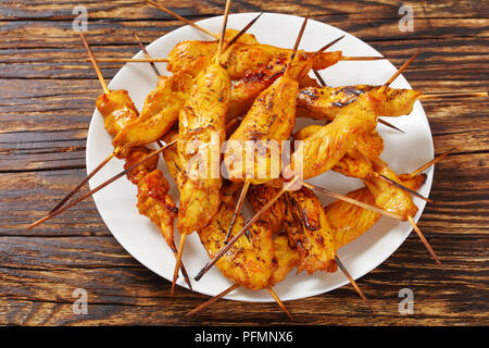 Close-up Chicken Satay auf Spieße auf einem weißen Teller auf Holztisch, klassisches Rezept, Ansicht von oben Stockfoto