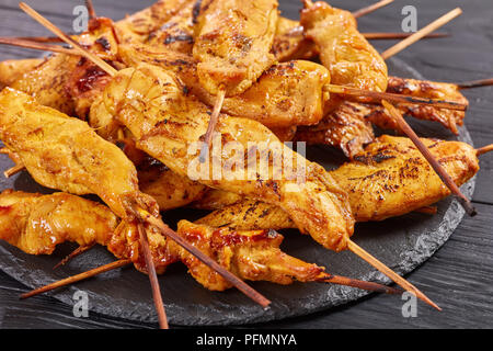 Chicken Satay auf Spieße auf einem schwarzem Schiefer Platte auf einen hölzernen Tisch, Blick von oben, in der Nähe Stockfoto