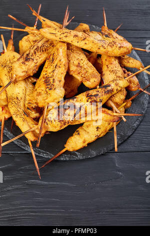 Gegrilltes Hühnchen satay auf Spieße auf einem schwarzen Stein Fach auf einem Holztisch, vertikale Ansicht von oben, in der Nähe Stockfoto