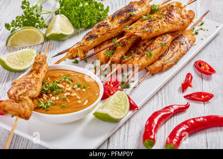 Chicken Satay auf Spieße bestreut mit fein gehackte Petersilie auf einem weißen rechteckigen Platte mit Erdnusssoße. rote Chilischoten, Kalk Schichten und Gleichheiten Stockfoto