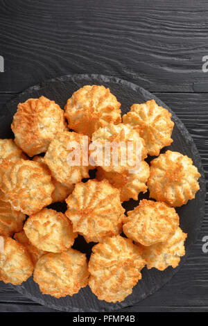 Leckere Kokosnuss Cookies auf einer Platte auf einem schwarzen Holztisch, vertikale Ansicht von oben Stockfoto