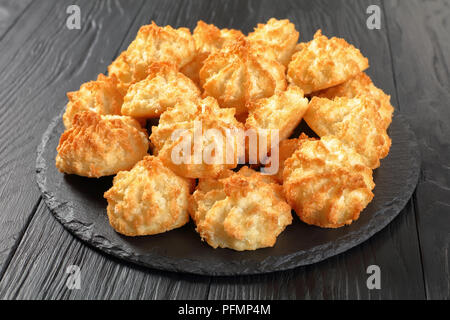 Leckere Kokosnuss Makronen Cookies auf einer Steinplatte auf einem schwarzen Holztisch, horizontale Ansicht von oben Stockfoto