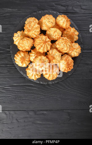 Leckere hausgemachte coconut Makronen cookies auf einem runden Schiefer Fach auf eine schwarze hölzerne Tabelle, Ansicht von oben Stockfoto