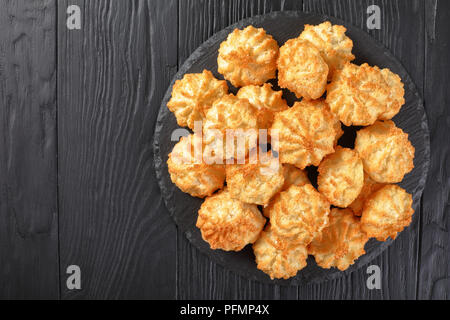 Leckere hausgemachte coconut Makronen Cookies auf einer Platte auf einem schwarzen Holztisch, horizontale Ansicht von oben, flach Stockfoto