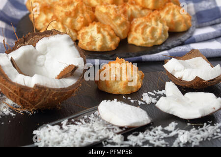 Leckere hausgemachte coconut Makronen Cookies auf einer Steinplatte auf einem schwarzen Holztisch mit Zutaten im Vordergrund, horizontale Ansicht von oben, Clos Stockfoto