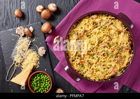 Tetrazzini - Spaghetti, Putenfleisch, geriebener Käse, grüne Erbsen, Champignons Auflauf in einer Auflaufform mit Zutaten im Hintergrund, amerikanische Küche, Stockfoto