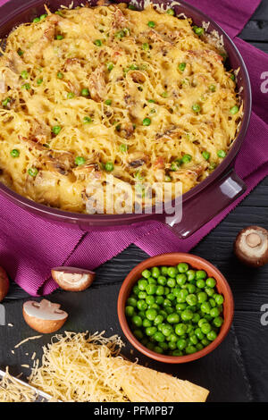 Tetrazzini - Pasta, Sahnesauce, Hühnerfleisch, geschmolzenem Käse, grüne Erbsen, Champignons Auflauf in einer Auflaufform mit Zutaten im Hintergrund, classic Stockfoto