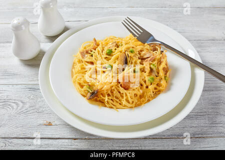 Teil der Köstlichen Tetrazzini - Pasta, Sahnesauce, Hühnerfleisch, geschmolzenem Käse, grüne Erbsen, Champignons Kasserolle auf einem weißen Teller mit silber Gabel, Stockfoto