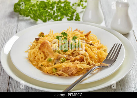 Teil der Tetrazzini - Pasta, Sahnesauce, Hühnerfleisch, geschmolzenem Käse, grüne Erbsen, Champignons Kasserolle auf einem weißen Teller mit silber Gabel, classic a Stockfoto