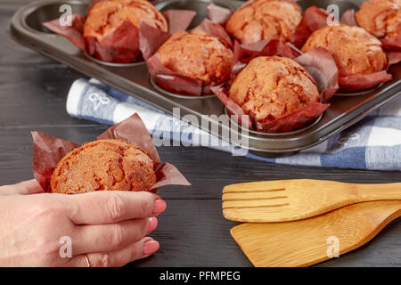 Frau hält frisch gebackenen Muffin. Muffins in einer Backform im Hintergrund, Ansicht von oben, close-up Stockfoto