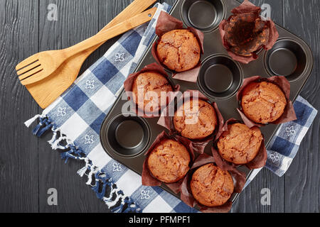 Frisch gebackene hausgemachte Muffins in einem Backblech mit Küchentuch auf schwarzem Holz- Tabelle, Ansicht von oben, flach Stockfoto