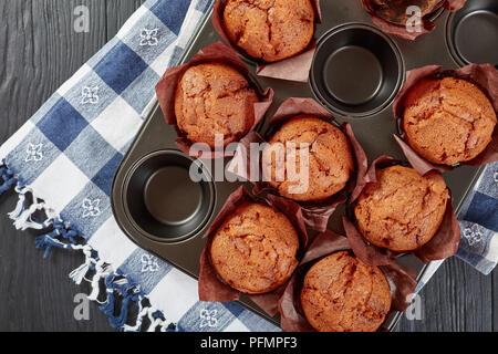 Frisch gebackene hausgemachte Muffins in einem Backblech mit Küchentuch auf schwarzem Holz- Tabelle, Ansicht von oben, flach, close-up Stockfoto