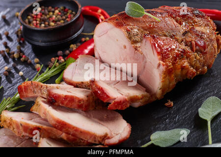 Lecker saftig gebratenes Stück Fleisch in Scheiben geschnitten auf schwarzem Schiefer Schneidebrett mit Messer, Chili, Pfeffer, frische Kräuter, Ansicht von Stockfoto